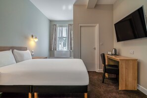 Une chambre d’hôtel comprenant un lit, un bureau avec une chaise, une télévision et une fenêtre avec des rideaux.