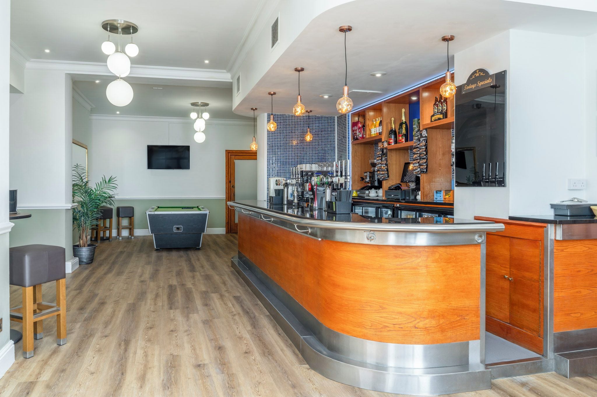 Un espace bar moderne avec un billard, un comptoir en bois et des lampes suspendues.
