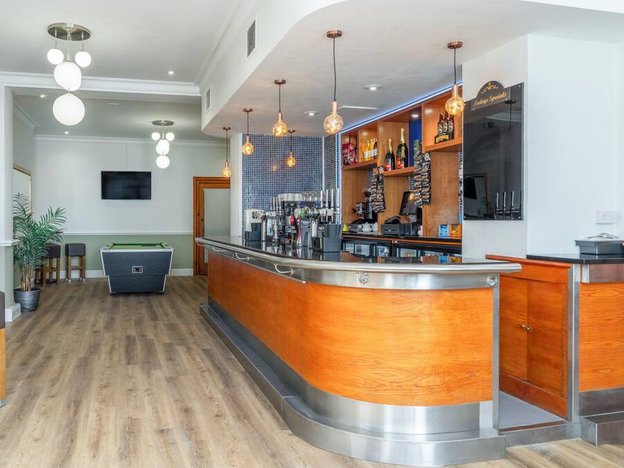 A modern bar area with a pool table, wooden bar counter, and hanging pendant lights.