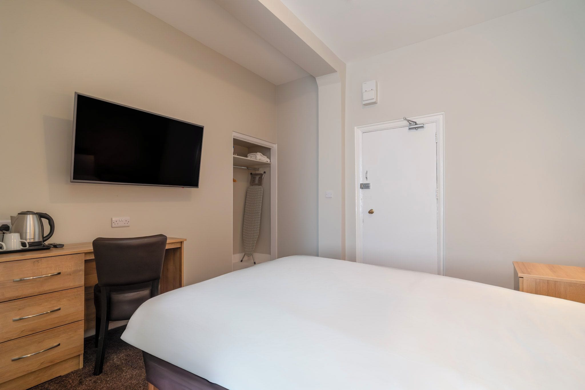 Una habitación de hotel con cama, escritorio, silla, televisor, armario y puerta.