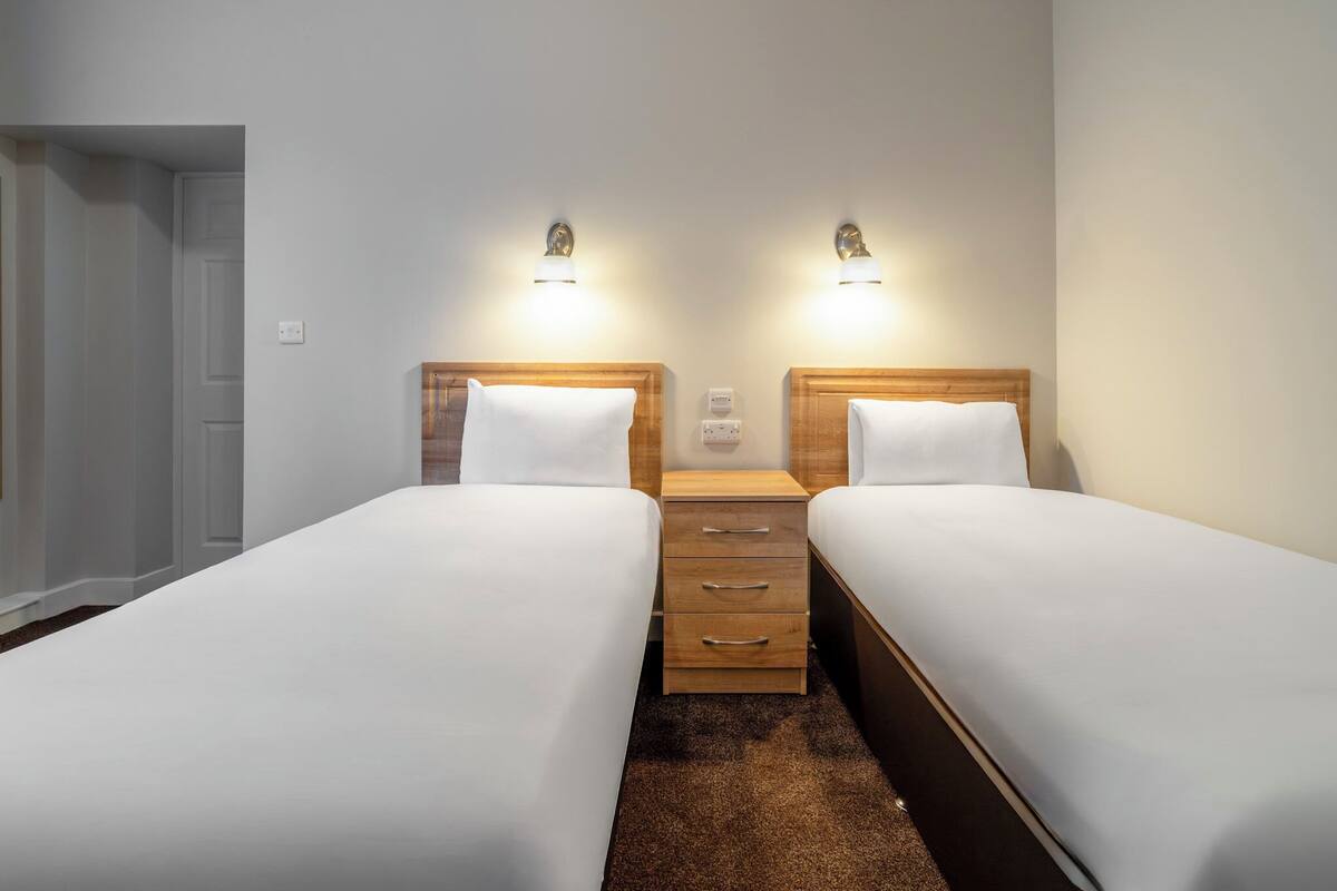 Ein Doppelzimmer mit zwei Betten, Holz-Kopfteilen, Nachttischen und Wandleuchten.