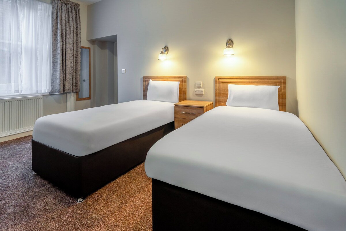 Une chambre d’hôtel avec deux lits, une table de chevet, un miroir et deux lampes fixées au mur.