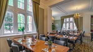 Een restaurantruimte in een hotel, met meerdere tafels, stoelen en grote ramen met gordijnen.