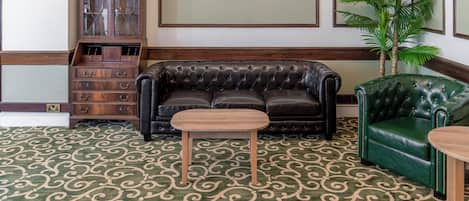 A room with a patterned carpet, a black leather sofa, a green armchair, a wooden cabinet, and a framed picture on the wall.