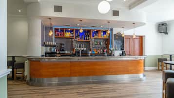 A bar area with a wooden counter, shelves with bottles, and hanging lights.