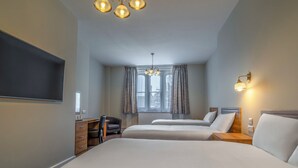 Een hotelkamer met twee bedden, een bureau, een stoel, een televisie en een raam met gordijnen.