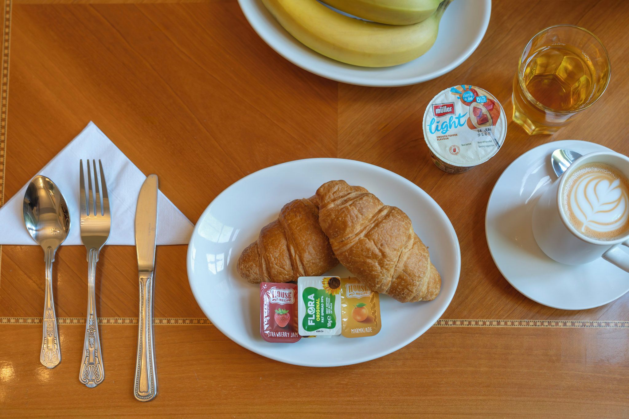 Mesa de madeira com croissants, iogurte e café para o pequeno-almoço.