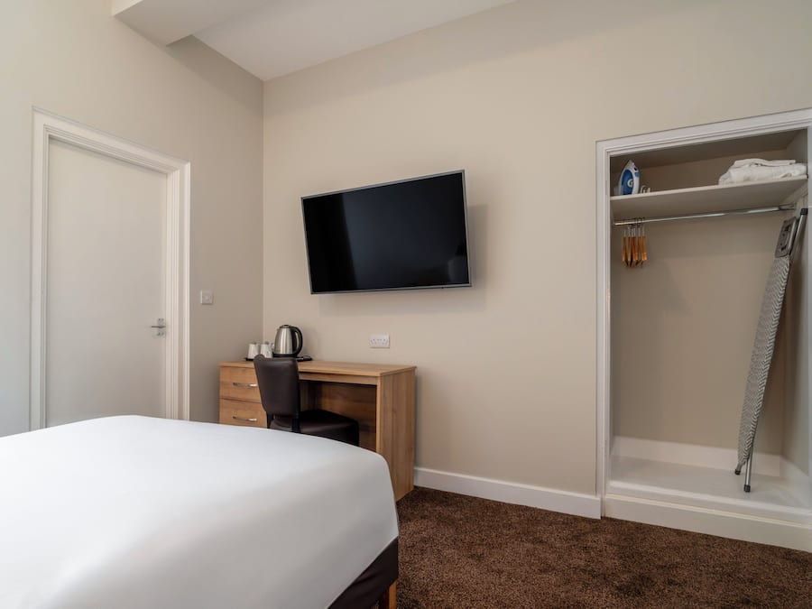 A hotel room with a bed, a desk with a chair, a television, and a walk-in closet with a shower.