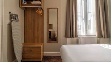 Een slaapkamer met een houten garderobe, een spiegel, een bed en een raam met gordijnen.