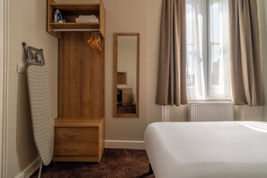Une chambre à coucher avec une armoire en bois, un miroir, un lit et une fenêtre avec des rideaux.