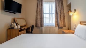 Hotellihuone, jossa on sänky, työpöytä tuolilla, televisio, ikkuna verhoilla ja yöpöytälamppu.