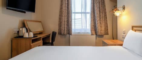 Habitación de hotel con cama, escritorio con silla, televisión, ventana con cortinas y lámpara de noche.