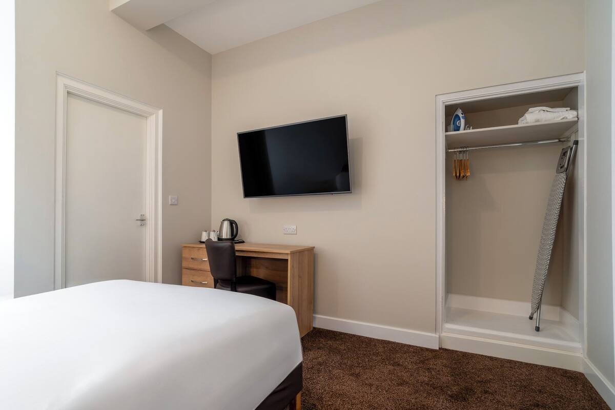 Ein Hotelzimmer mit einem Bett, einem Schreibtisch mit Stuhl, einem Fernseher und einem Ankleidezimmer mit Dusche.