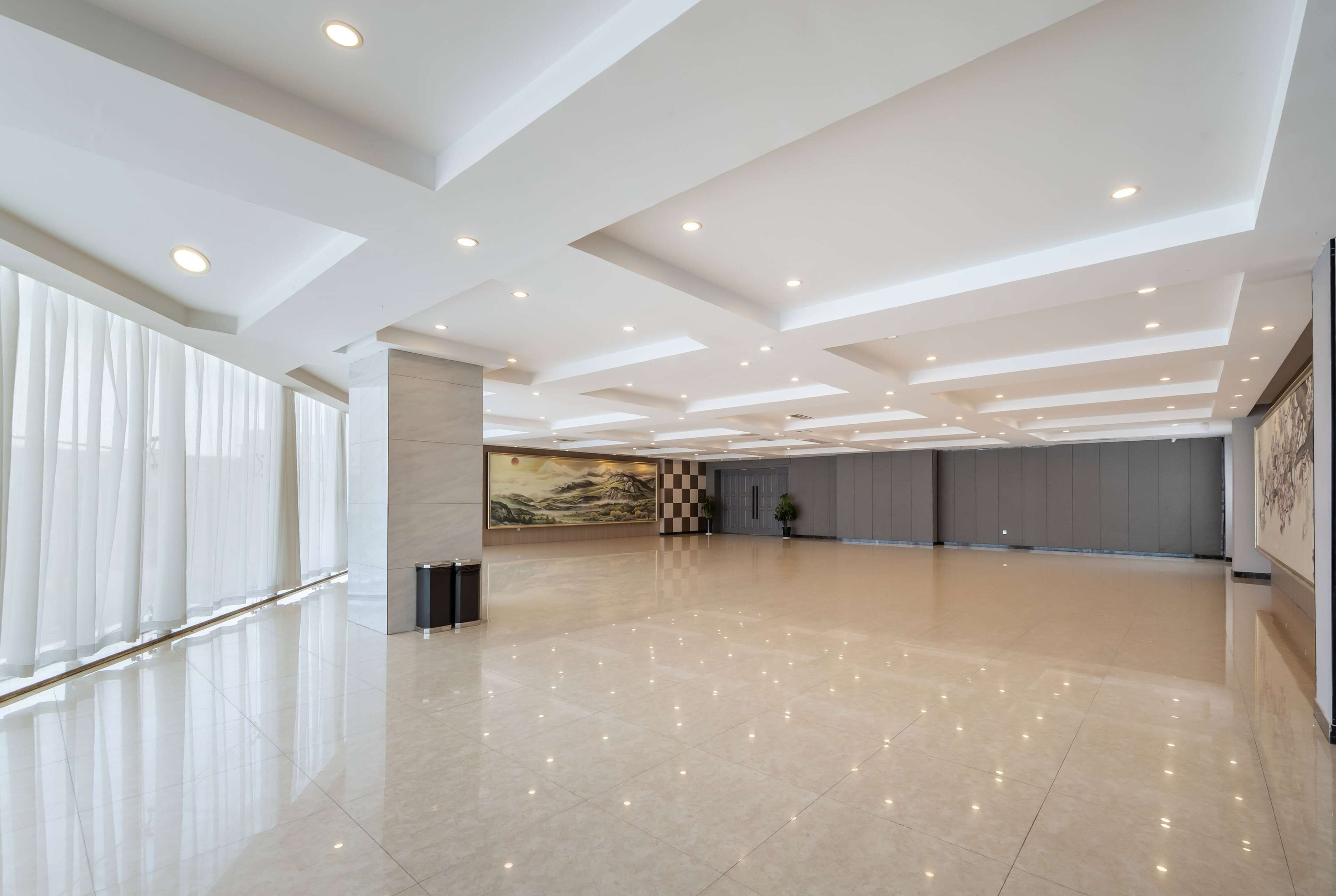 A spacious, modern hotel lobby with a high ceiling, recessed lighting, and a polished floor.