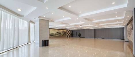 A spacious, modern hotel lobby with a high ceiling, recessed lighting, and a polished floor.