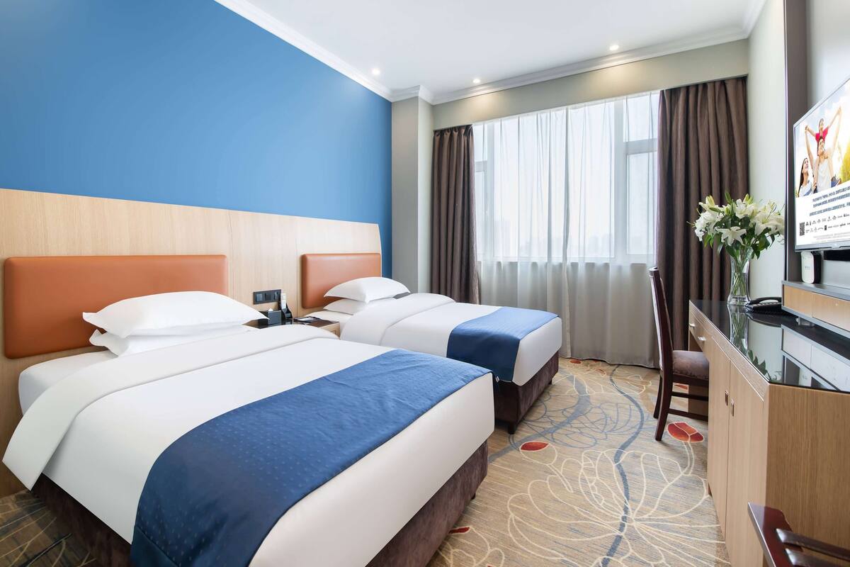 Habitación de hotel con dos camas, un escritorio, una silla, un televisor y una ventana con cortinas.