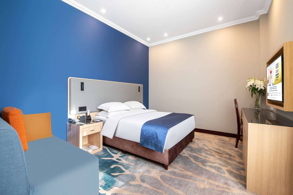 Una habitación de hotel con una cama grande, un escritorio, una silla y una mesita con un florero.