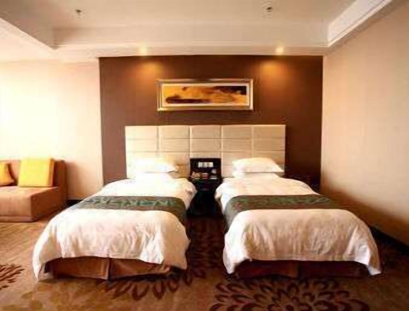 Quarto de hotel com duas camas, cabeceira, mesa de cabeceira, abajur e um quadro na parede.