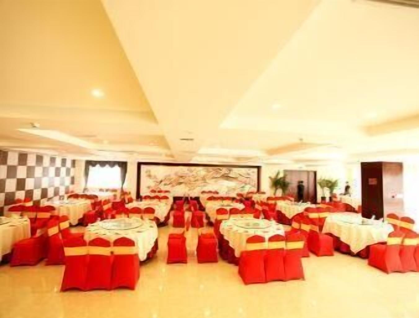 A banquet hall with round tables and red chairs, featuring a checkered wall pattern and a large abstract painting.