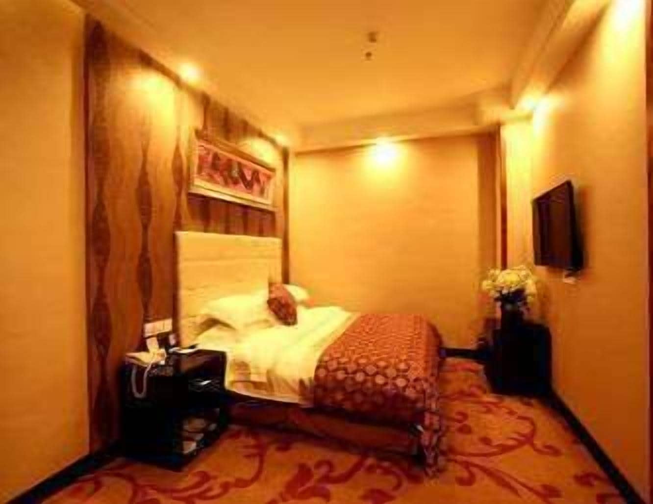 A hotel room with a bed, a nightstand, a vase with flowers, and a wall-mounted TV.