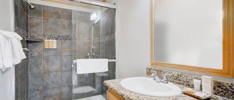 A modern bathroom with a glass-enclosed shower, a white sink, and a wooden vanity.