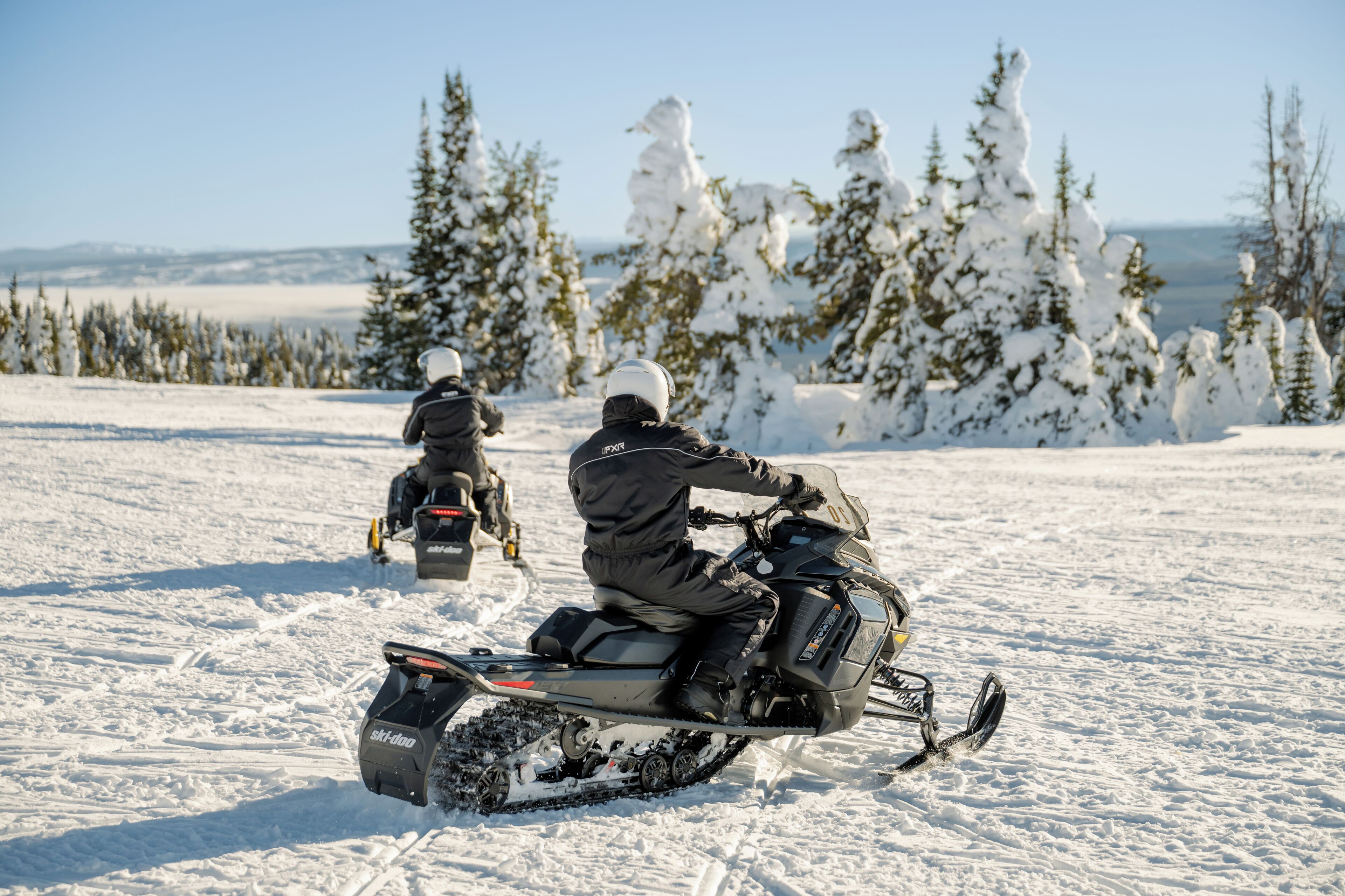 A snowmobile on a snowy landscape with trees and a clear sky.