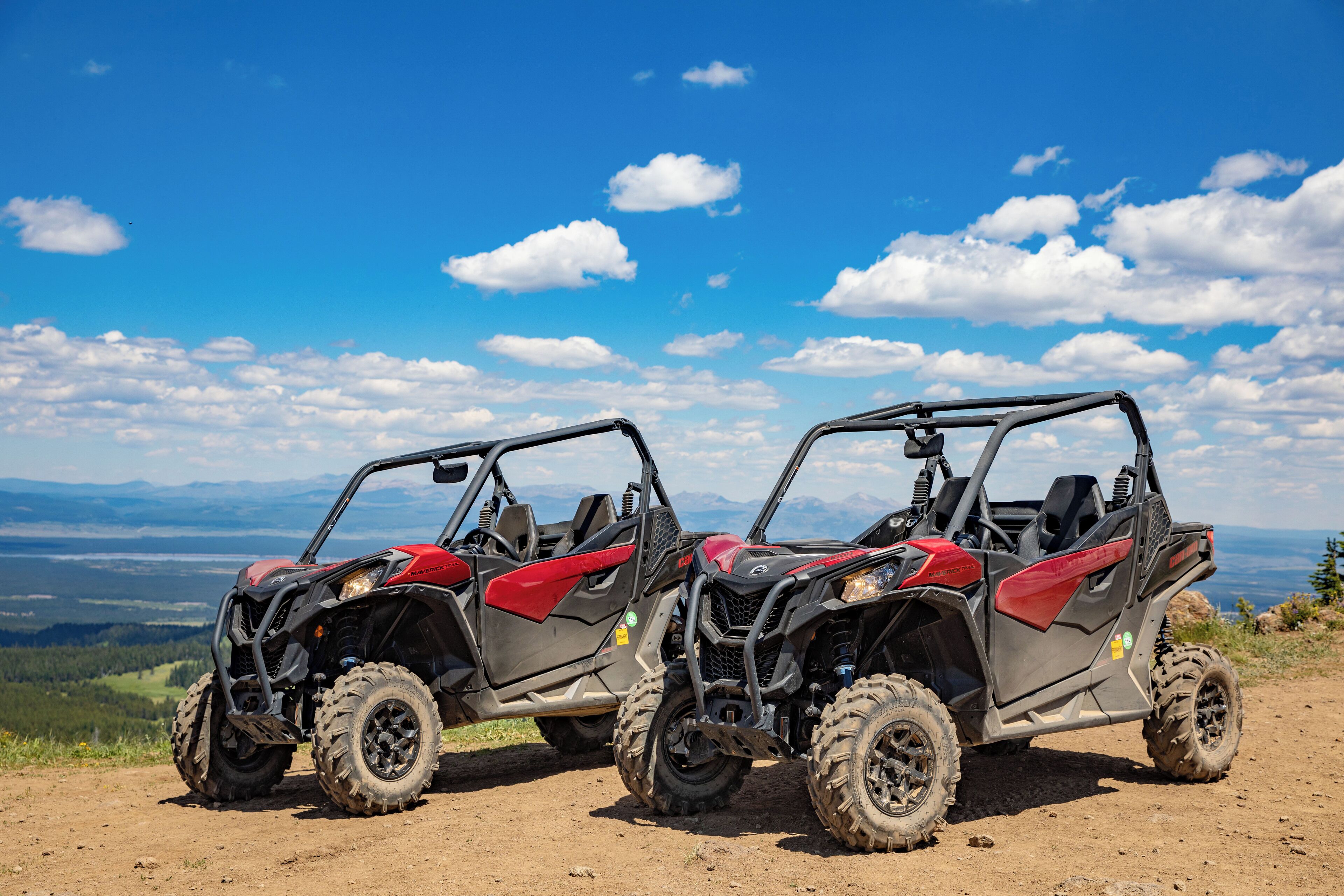 Two off-road vehicles parked on a dirt path with a scenic view of mountains and a clear blue sky.