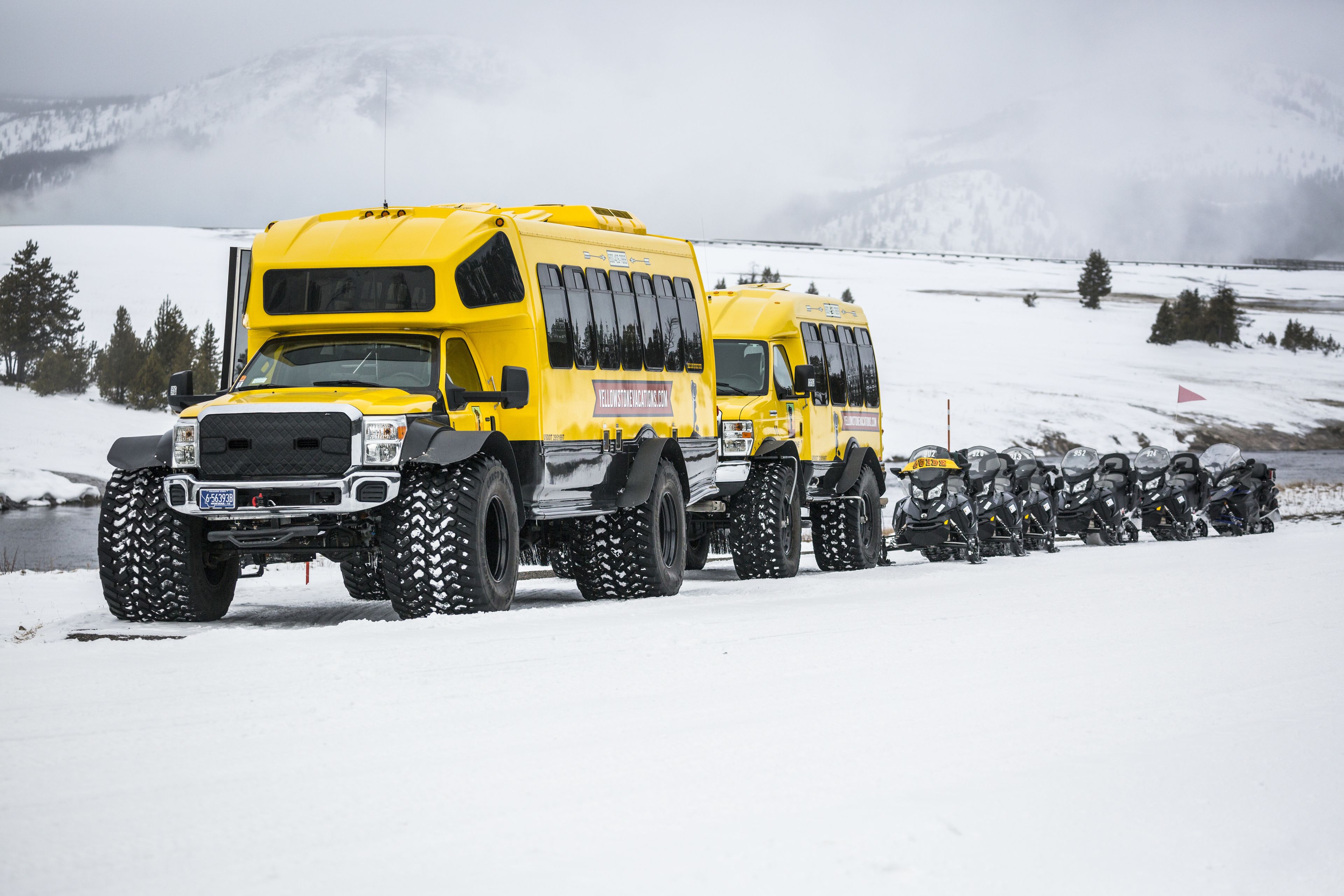 A yellow bus with large tires parked on a snowy road.