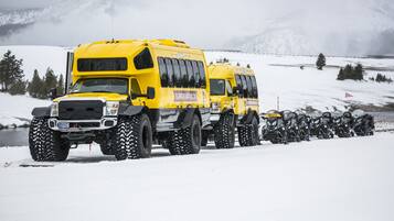 A yellow bus with large tires parked on a snowy road.