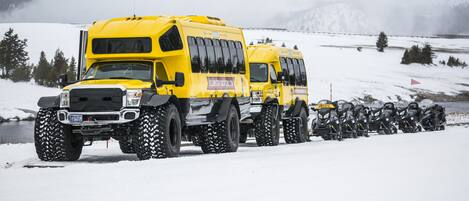 A yellow bus with large tires parked on a snowy road.