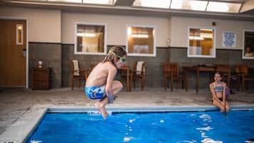 Una piscina con un trampolín, sillas y una mesa al fondo.