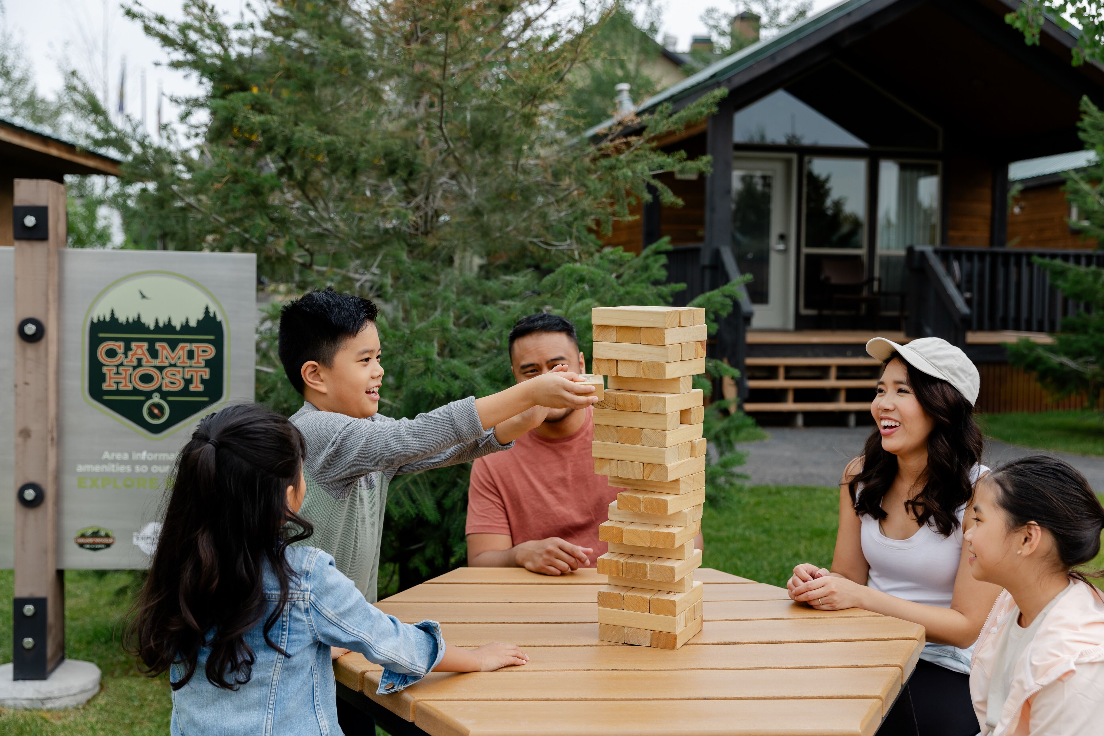 A group of people playing a game of Jenga at a wooden table outdoors.