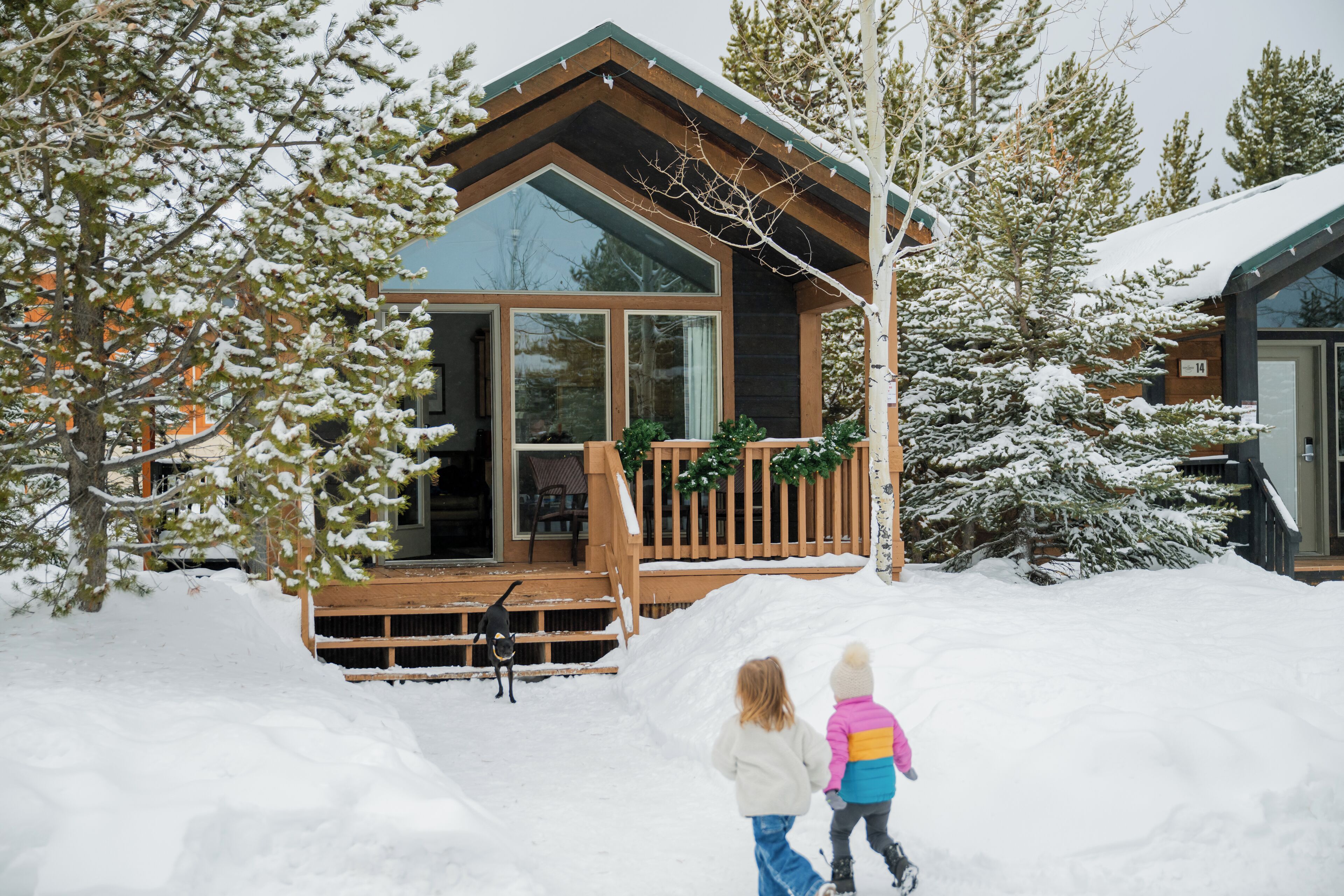 Une cabane en bois dotée d’une grande porte vitrée et d’une terrasse, entourée d’arbres couverts de neige.