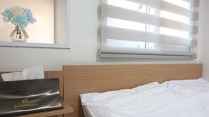 A neatly made bed with white linens, a wooden headboard, a bedside table with a black bag labeled "guesthouse," and a window with blinds partially open. - 24guesthouse Seoul Station (Seoul)