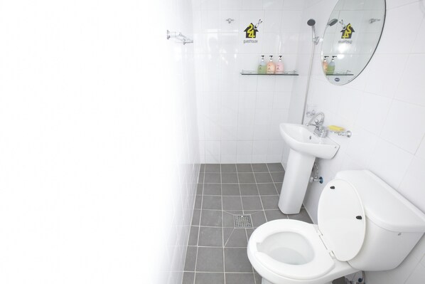 Ein Badezimmer mit Toilette, Waschbecken und Dusche. Auf dem Regal befinden sich Pflegeprodukte.