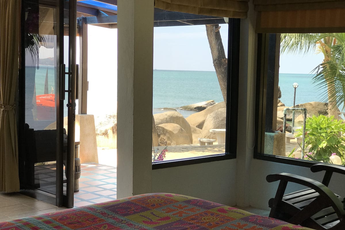 Una habitación con cama, una silla y vistas al océano a través de amplios ventanales.