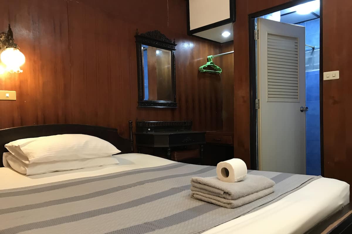 Habitación de hotel con cama, mesita de noche, espejo, un perchero verde y puerta al baño.