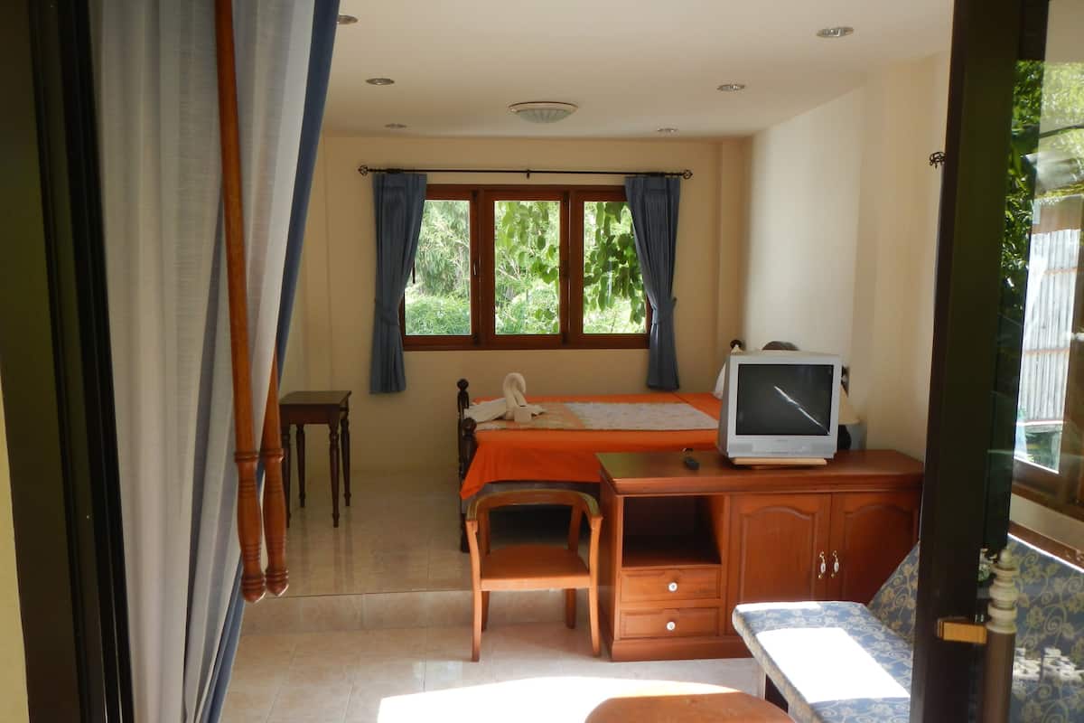 Una habitación con cama, escritorio con computadora, silla, una mesita y ventana con cortinas.