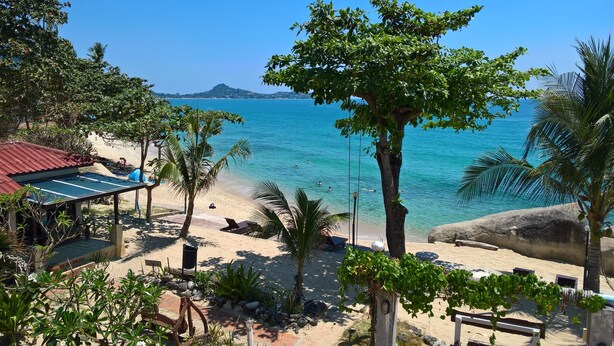 A beach with a wooden structure, palm trees, and a view of the ocean. - Sunrise Bungalow (Koh Samui)