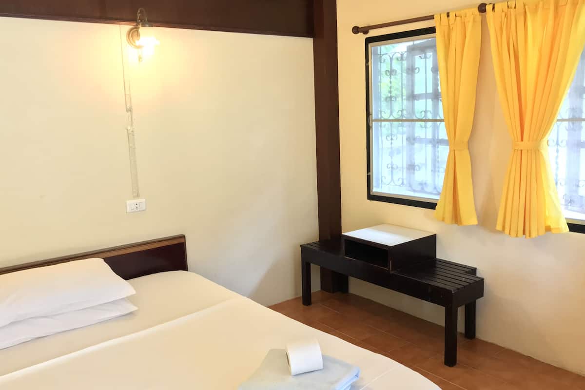 Habitación de hotel con cama, mesita de noche, lámpara, ventana con cortinas amarillas y vistas al exterior.
