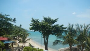 A beach view with a large tree, palm trees, and a sandy area with outdoor seating. - Sunrise Bungalow (Koh Samui)