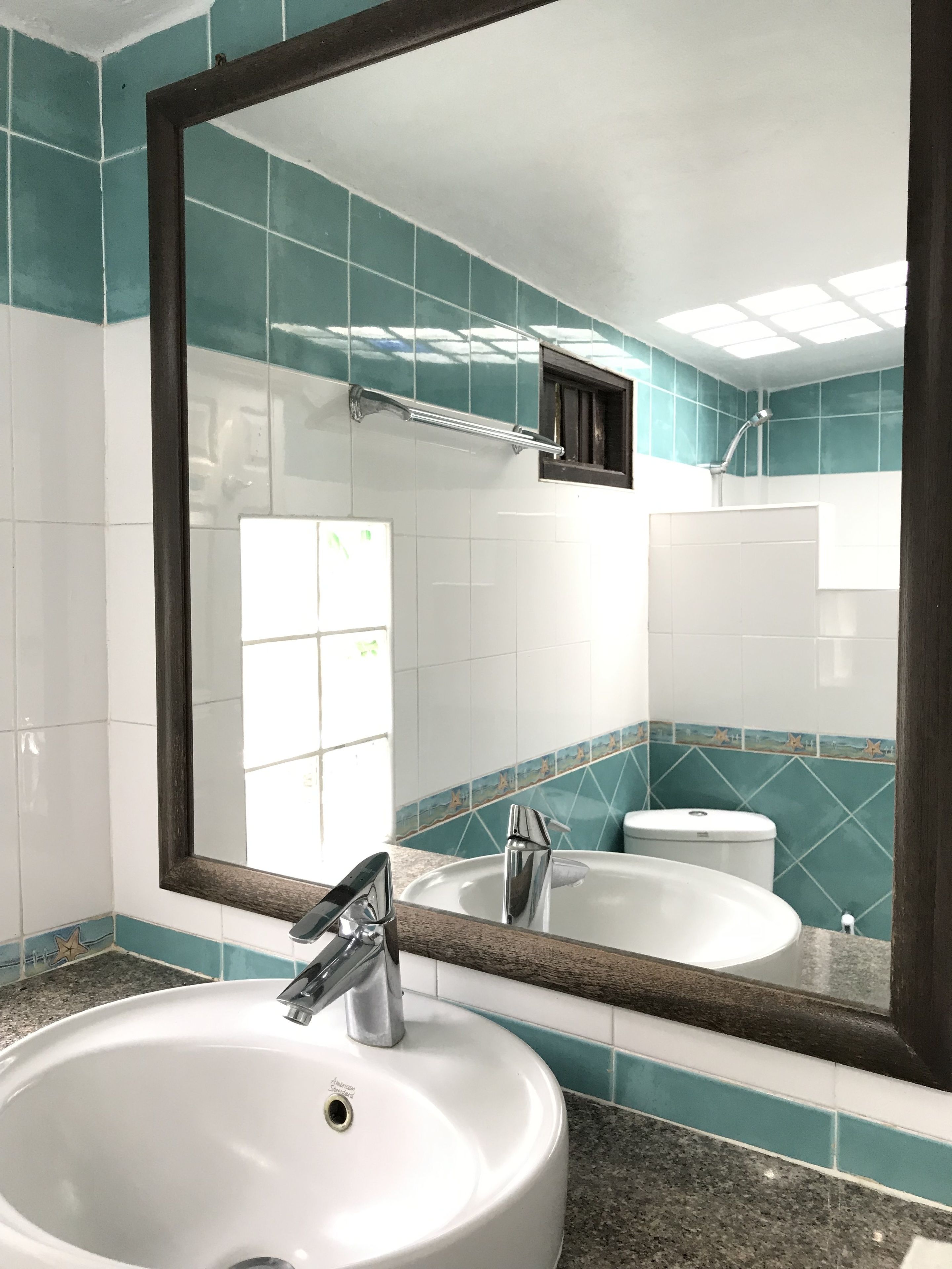 Une salle de bain avec un lavabo blanc, un miroir et des carreaux de couleur turquoise et blanche.