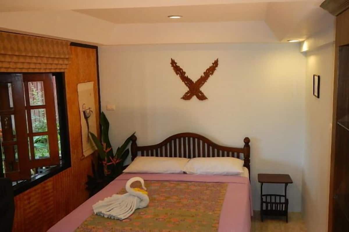 Un dormitorio con una cama de madera, un adorno en la pared, una mesita y una ventana con cortinas.