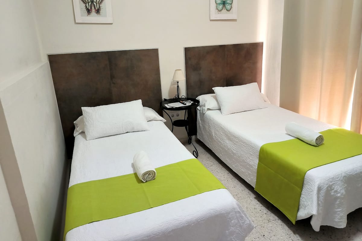 Two single beds with white linens and green bedspreads, a nightstand with a lamp, and butterfly artwork on the walls.