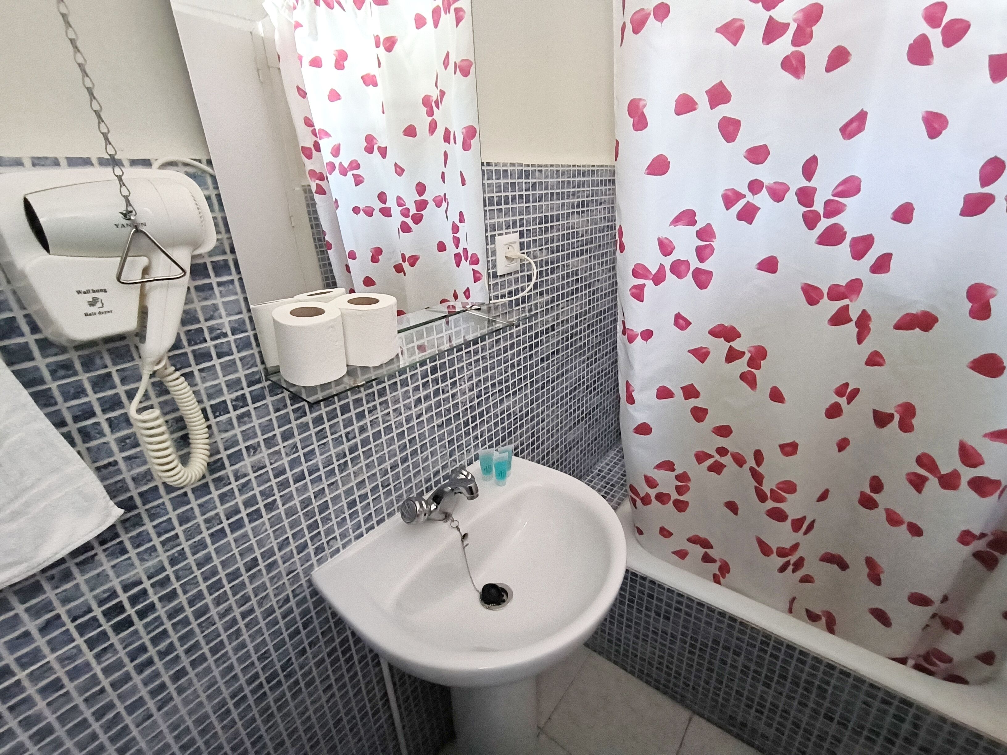 A bathroom with a white sink, a towel rack, a toilet paper holder, and a shower curtain with a rose pattern.