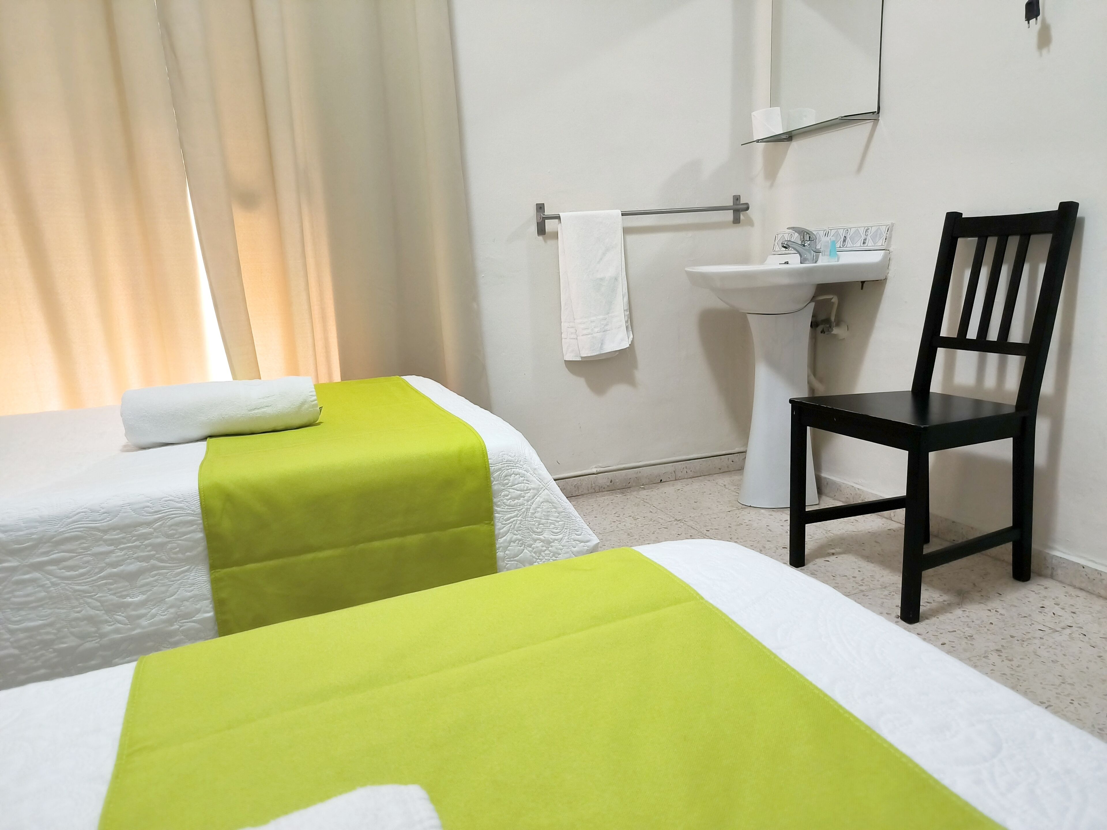 Habitación de hotel con dos camas, una silla, un lavamanos y un espejo.