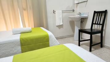 Habitación de hotel con dos camas, una silla, un lavamanos y un espejo.
