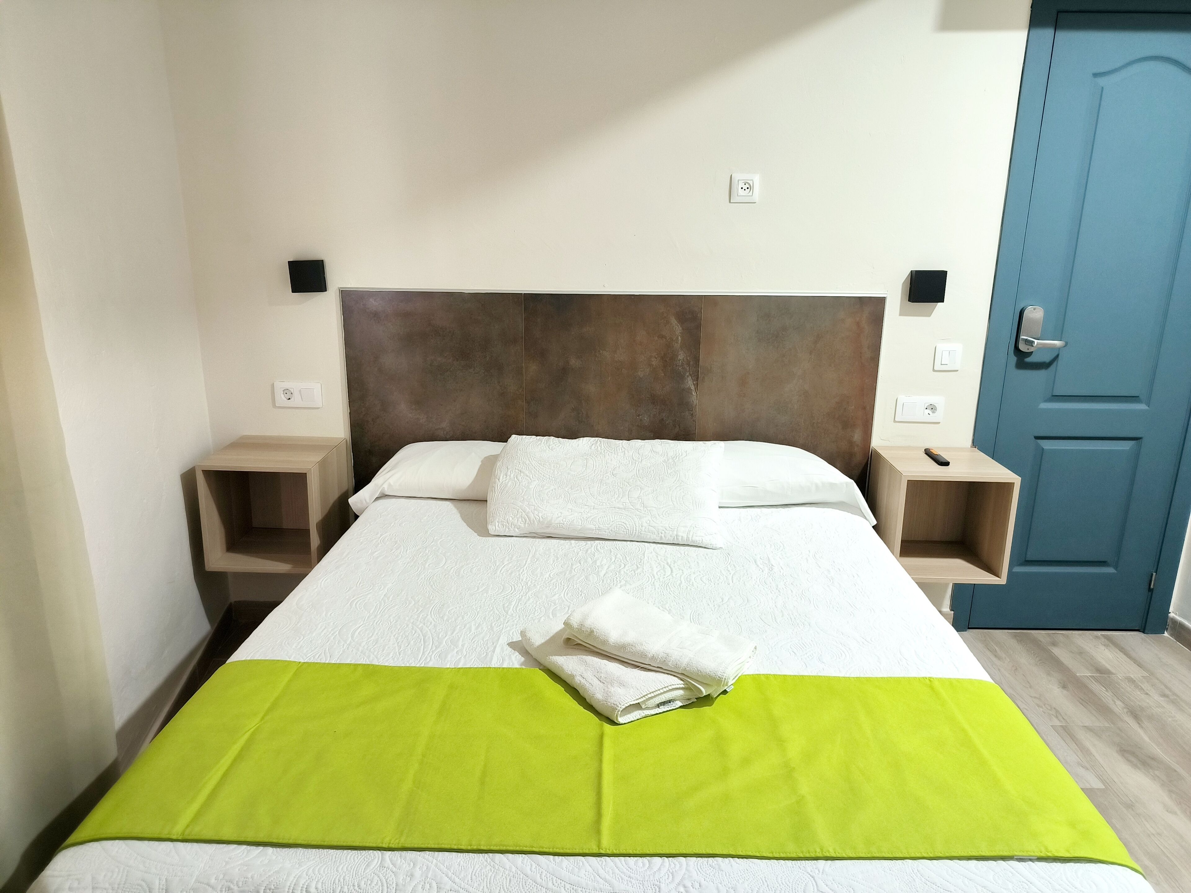 A neatly made bed with a green blanket, a wooden headboard, and bedside tables with lamps.