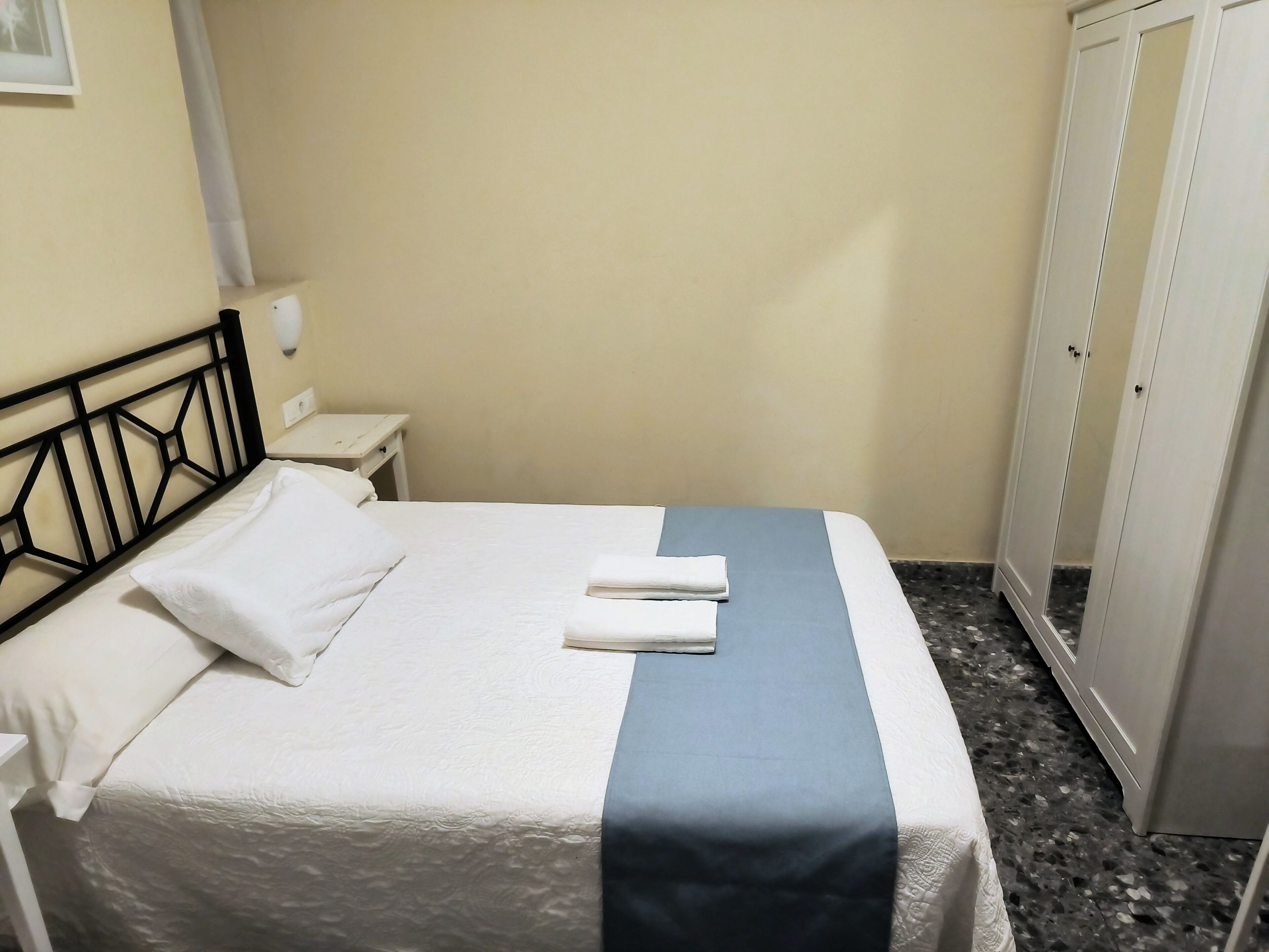 A neatly made bed with white linens and a blue accent, a white nightstand with a lamp, and a wardrobe with mirrored doors.