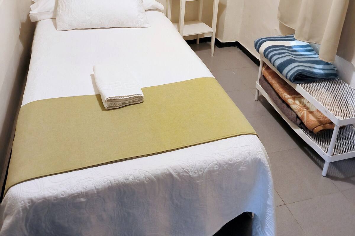 A neatly arranged hotel room with a bed, a bedside table, a small white cabinet, and a hanging coat rack.